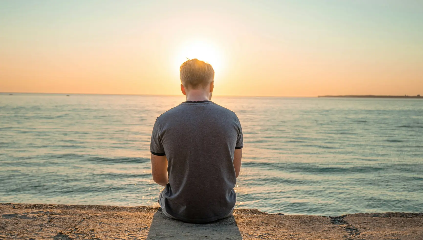 man sitting on sand front of sea during golden hour